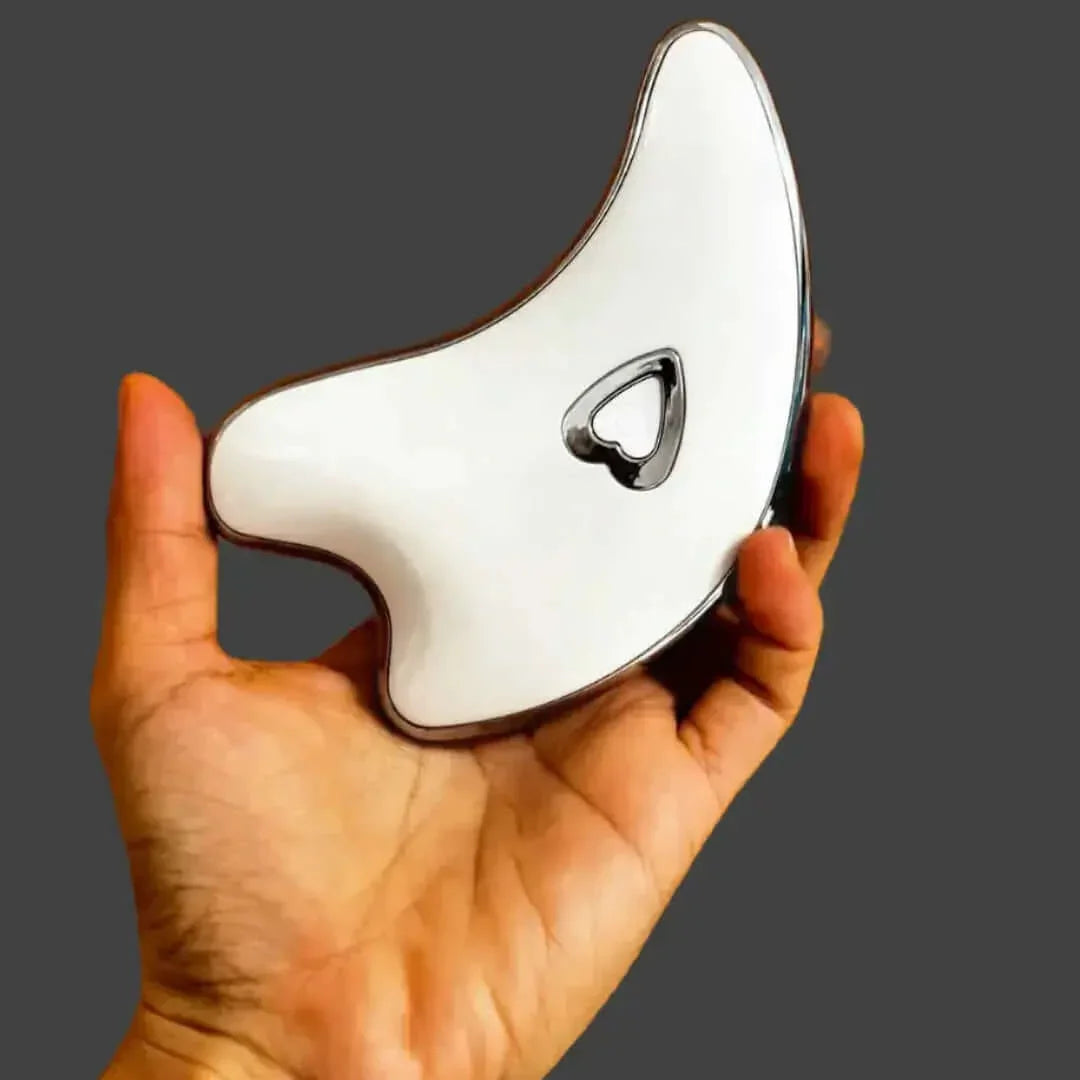 Hand holding a white gua sha facial massage tool with heart-shaped cutout on grey background