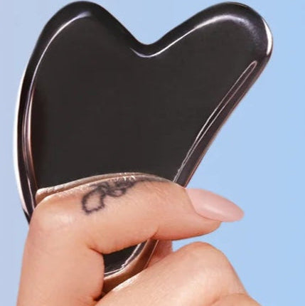 Hand holding a black Gua Sha tool against a blurred background